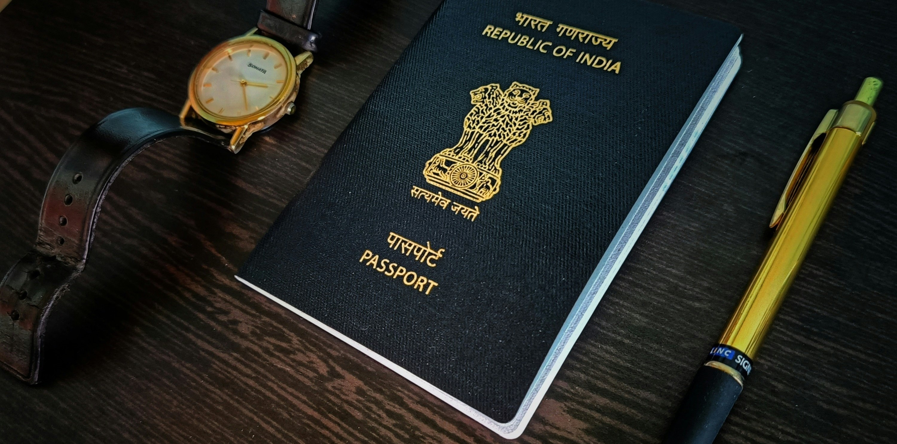 An Indian passport, wristwatch and pen on a wooden table